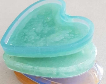 May include: A stack of four heart-shaped coasters in shades of blue, green, purple, and yellow. The coasters are made of resin and have a glossy finish.