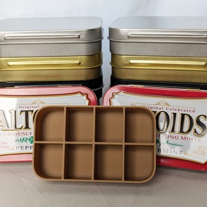 May include: Two vintage Altoids mint tins, one red and one blue, with the original packaging. The tins are open and a brown plastic tray with eight compartments is in the middle of the image.