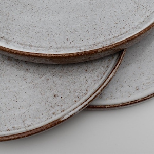 Könnte beinhalten: Drei weiße Keramikteller mit braunen Rändern, die übereinander gestapelt sind. Die Teller haben eine gesprenkelte Textur.