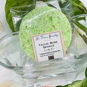 Puede incluir: Esponja verde para mascarilla facial en una bolsa de plástico transparente. La esponja es texturizada y tiene una etiqueta que dice "Vi Tare's Bounty Facial Mask Sponge Gently Firm To Remove Masks & Cleanse Skin Made with natural cellulose."