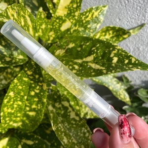 May include: A clear plastic tube with a white applicator tip filled with a yellow liquid. The tube is being held by a hand with red nail polish.
