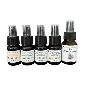 Op de afbeelding: Vijf bruine glazen spuitflessen met zwarte doppen en etiketten. De etiketten zijn wit met zwarte tekst en tonen verschillende geuren: Lebensfreude, Geistge Klarheit, Tannenwald, Gute-Nacht en Zirbenspray. De flessen zijn 30 ml of 50 ml.