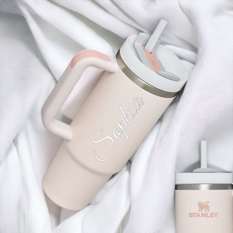 Pu&ograve; includere: Un bicchiere isolante rosa chiaro con coperchio bianco e manico. Il bicchiere ha una cannuccia e il nome "Sophia" &egrave; scritto sul lato. Il bicchiere &egrave; alto circa 25 cm.