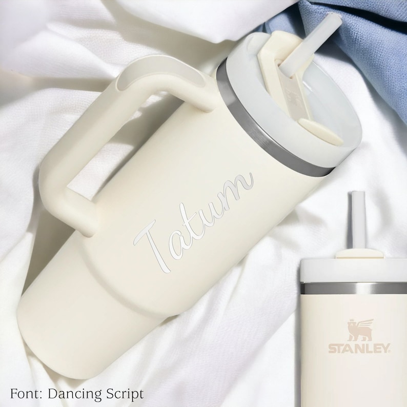Pu&ograve; includere: Bicchiere termico color crema con manico, cannuccia e coperchio. Il nome "Tatum" &egrave; inciso sul lato in corsivo. &Egrave; visibile anche un bicchiere pi&ugrave; piccolo abbinato, con il logo "Stanley".