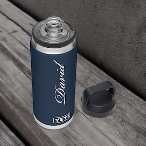 Puede incluir: Una botella de agua aislada azul marino con el nombre "David" en escritura blanca. La botella tiene una tapa transparente y una tapa negra. La marca "YETI" est&aacute; impresa en la parte inferior.