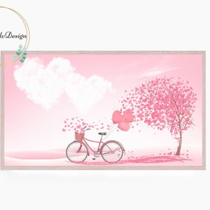 May include: A pink watercolor print featuring a bicycle with a basket, heart-shaped balloons, and a tree with heart-shaped leaves. The background is a soft pink with heart-shaped clouds. The artwork is framed with a light wood frame.