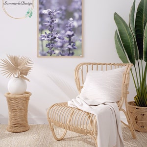 Puede incluir: Una impresi&oacute;n enmarcada de un primer plano de flores moradas con un fondo borroso. La impresi&oacute;n est&aacute; colgada en una pared blanca sobre una silla de mimbre con una manta blanca.