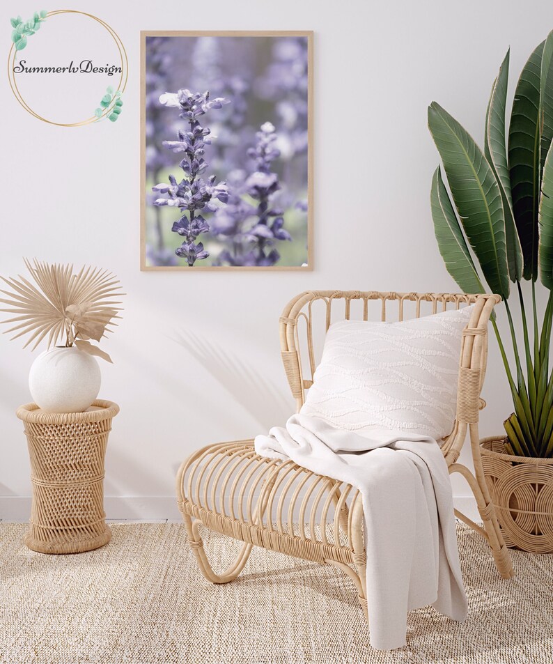 Puede incluir: Una impresi&oacute;n enmarcada de un primer plano de flores moradas con un fondo borroso. La impresi&oacute;n est&aacute; colgada en una pared blanca sobre una silla de mimbre con una manta blanca.