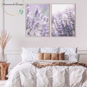 Puede incluir: Dos impresiones enmarcadas de flores de lavanda en un ambiente de dormitorio. Las impresiones est&aacute;n colgadas en una pared blanca sobre una cama con ropa de cama blanca y almohadas marrones.