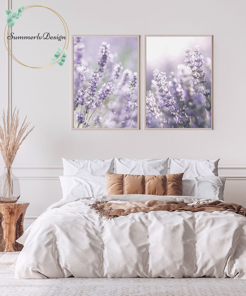 Puede incluir: Dos impresiones enmarcadas de flores de lavanda en un ambiente de dormitorio. Las impresiones est&aacute;n colgadas en una pared blanca sobre una cama con ropa de cama blanca y almohadas marrones.