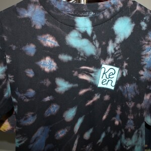 May include: Black tie-dye t-shirt with a blue and white square logo that says "Ken" in a white font.