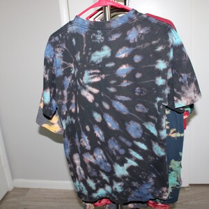 May include: A black tie-dye t-shirt with blue, teal, and pink accents. The shirt has a circular pattern with a darker center and lighter edges.