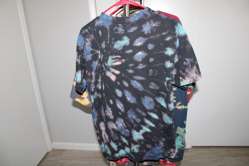 May include: A black tie-dye t-shirt with blue, teal, and pink accents. The shirt has a circular pattern with a darker center and lighter edges.