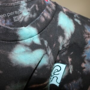May include: Black tie-dye t-shirt with a blue and green logo that says "keen persp" on the front.