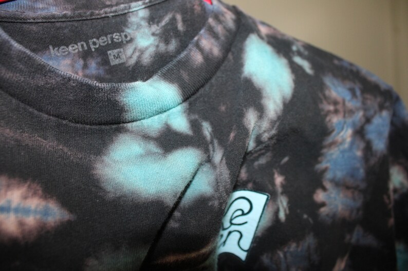 May include: Black tie-dye t-shirt with a blue and green logo that says "keen persp" on the front.
