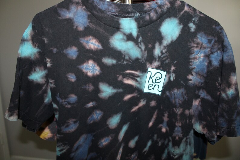 May include: Black tie-dye t-shirt with a blue and white square logo that says "Ken" in a white font.