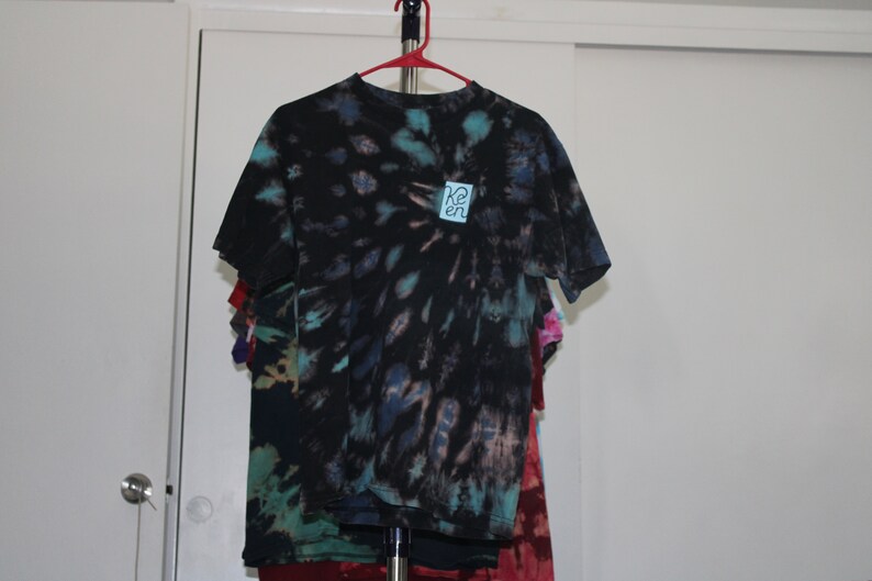 May include: A black tie-dye t-shirt with a blue and white square patch that says "Re:en" on it.