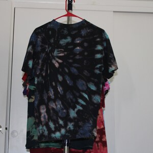 May include: A black tie-dye t-shirt with blue, green, and pink accents. The shirt is hanging on a hanger.