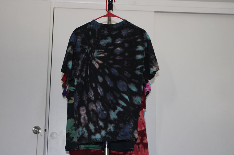 May include: A black tie-dye t-shirt with blue, green, and pink accents. The shirt is hanging on a hanger.