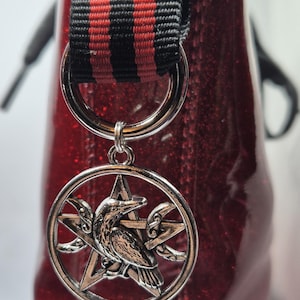 May include: Red glitter boot with a black and red striped strap and a silver charm featuring a raven and a pentagram.