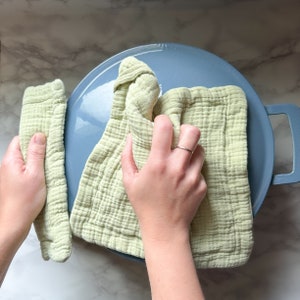 May include: A person is using a light green dishcloth to wipe down a blue ceramic pot. The dishcloth is folded in half and the person is holding it with both hands.