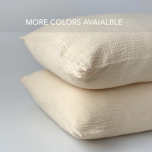 May include: Two cream-colored square pillows stacked on top of each other. The pillows have a textured, grid-like pattern. The text "MORE COLORS AVAIALBLE" is visible at the top of the image.