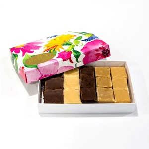 May include: A white box with a floral design lid open to reveal a box of fudge. The fudge is arranged in rows of alternating chocolate and vanilla squares. The box is labeled "Hall's Candies".