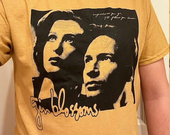 May include: Mustard yellow t-shirt featuring a black and white graphic of two people and the text "gin blossoms". The shirt also has the text "anywhere you go, I'll follow you down."
