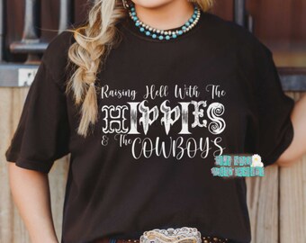 May include: A black t-shirt with white text that reads "Raising Hell With The Hippies & The Cowboys".