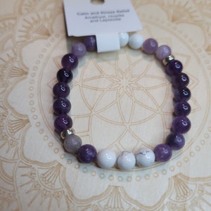 May include: A purple, white, and gray gemstone bracelet with a tag that reads "Calm and Stress Buster Amethyst, Howlite and Lepidolite".