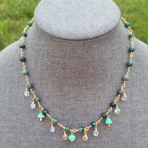 May include: A gold-toned necklace with green and clear beads. The necklace features a series of round, dark green beads connected by gold wire. Small, clear, and green beads dangle from the necklace, creating a delicate, eye-catching design.