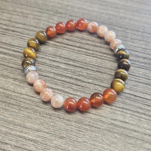 May include: A multi-colored beaded bracelet with brown, orange, and pink beads. The bracelet has silver accents.