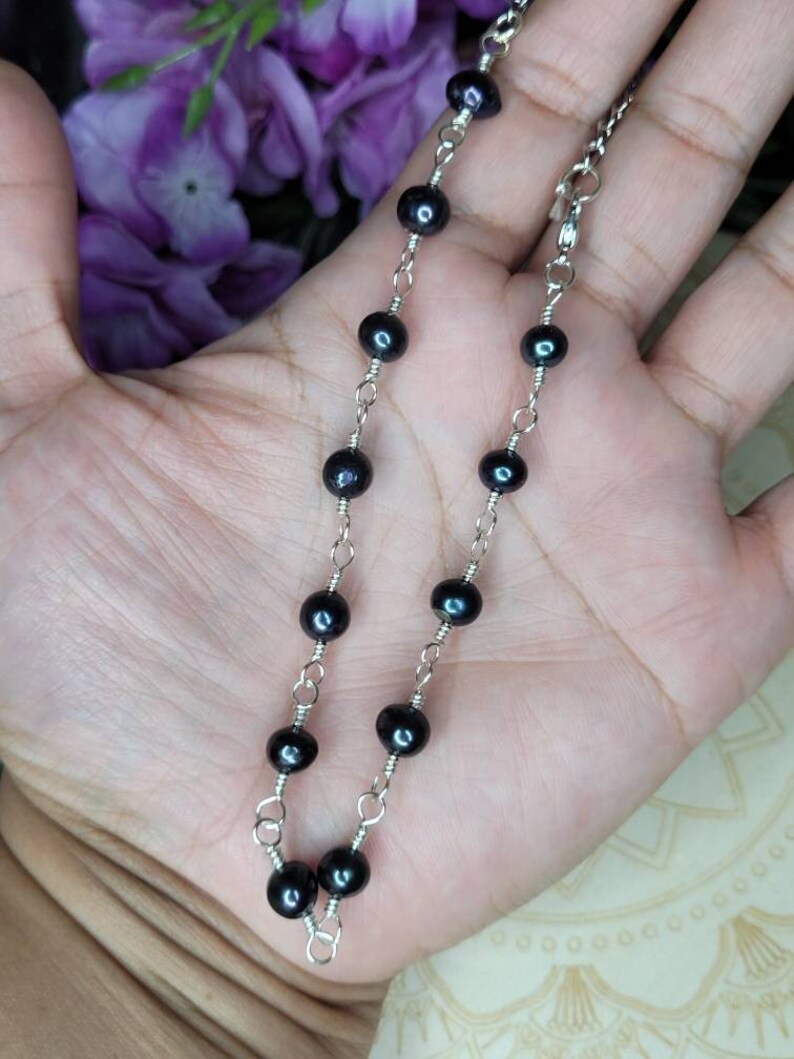 May include: A delicate silver chain necklace with black pearl beads. The necklace is approximately 18 inches long and features a lobster clasp closure.