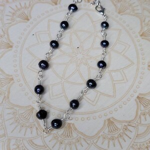 May include: A delicate silver chain bracelet with black pearls. The bracelet is made with small, round pearls and a silver chain.