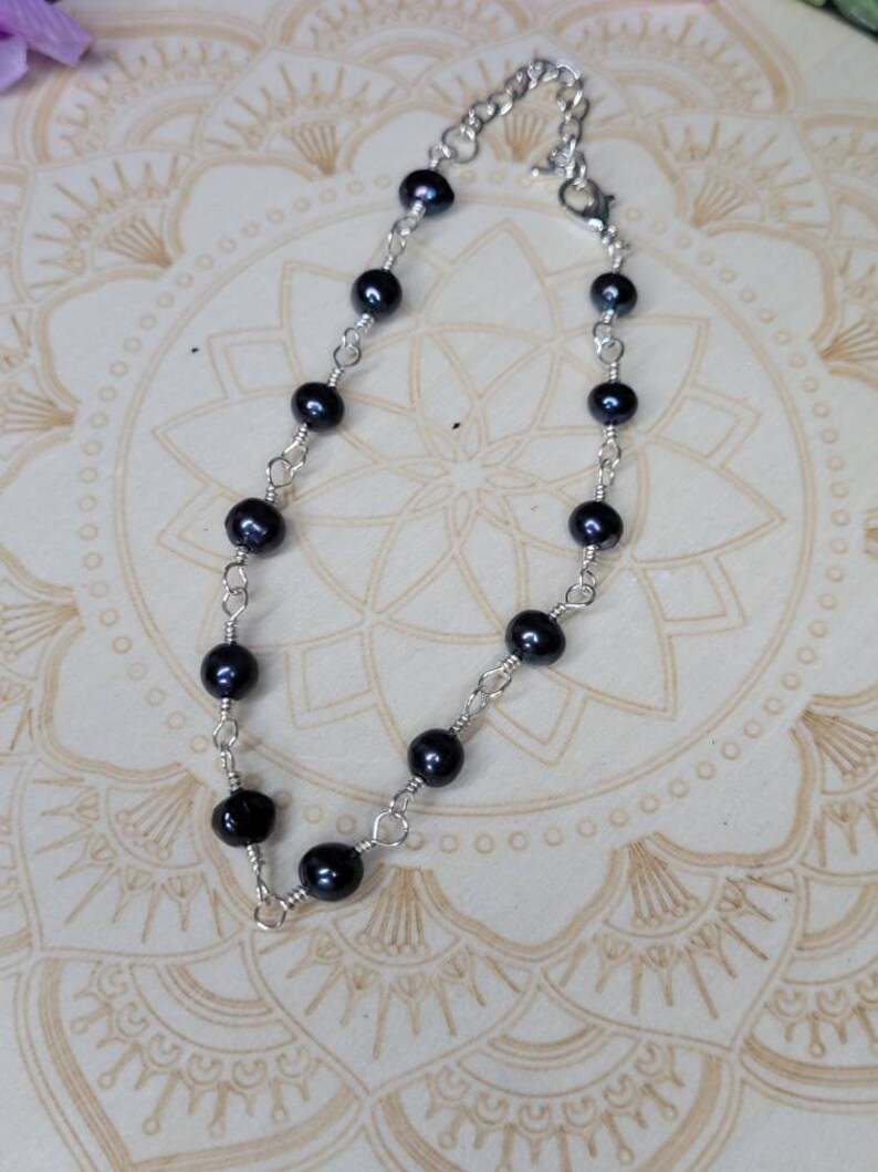 May include: A delicate silver chain bracelet with black pearls. The bracelet is made with small, round pearls and a silver chain.