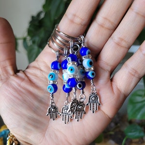 May include: Five silver keychains with blue and white evil eye beads and silver hamsa hand charms.