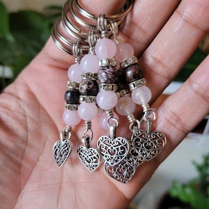 May include: Five pink and brown beaded keychains with silver heart charms. Each keychain has a silver ring and is made with pink and brown beads.