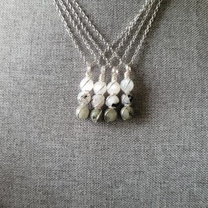 May include: Four silver necklaces with gemstone pendants. Each necklace has a delicate chain and a pendant made of white, black, and gray stones. The pendants are wire-wrapped and arranged in a vertical line.