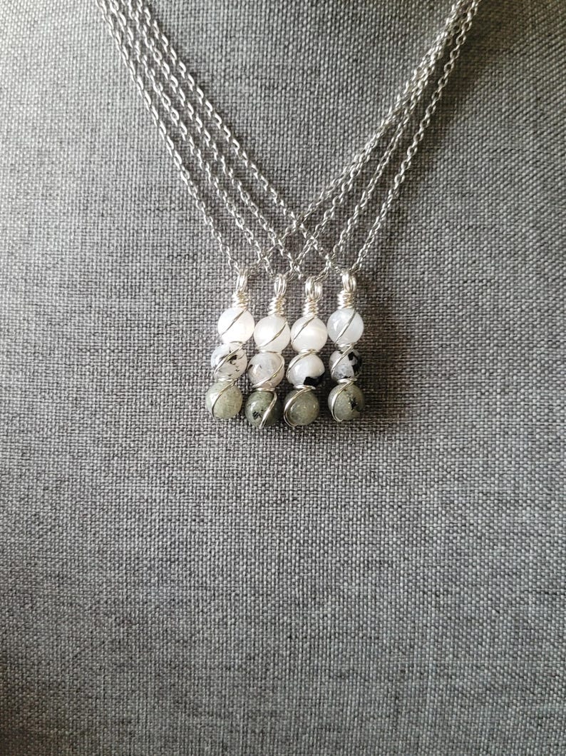 May include: Four silver necklaces with gemstone pendants. Each necklace has a delicate chain and a pendant made of white, black, and gray stones. The pendants are wire-wrapped and arranged in a vertical line.