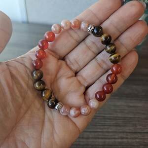 May include: A bracelet made with carnelian, tiger's eye, and sunstone beads. The beads are separated by silver spacers.