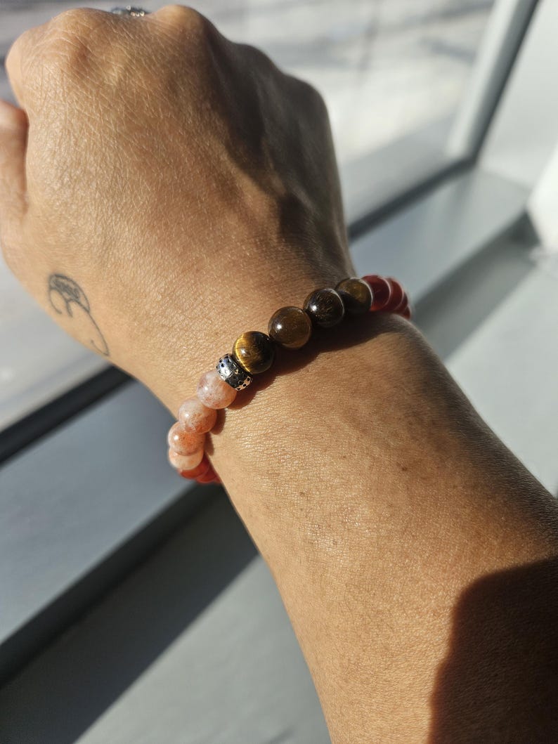 May include: A beaded bracelet with a silver charm, featuring orange, brown, red, and pink stones.