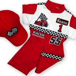 May include: A red racing-themed outfit set with a matching baseball cap. The outfit includes a red and white jumpsuit with "RACER" and "55" patches, and a red cap with checkered flag emblems. The jumpsuit features a race car graphic and the name "Keanu".