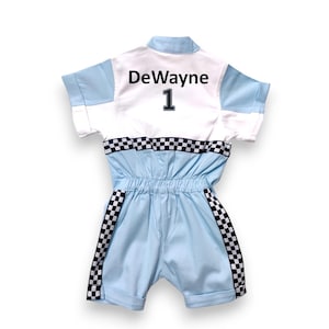 May include: A light blue jumpsuit with a white panel on the back. The panel has the name "DeWayne" and the number "1" in black. The jumpsuit has black and white checkered trim on the sleeves and legs.