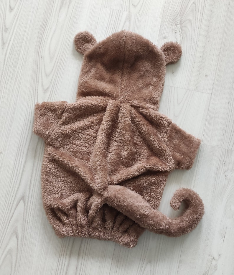 Puede incluir: Un disfraz de mono de peluche marr&oacute;n con capucha y cola. El disfraz est&aacute; hecho de tela suave y peluda.
