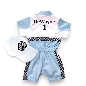 May include: A white and light blue racing jumpsuit with a black checkered trim. The jumpsuit has the name "DeWayne" and the number "1" on the back. A white baseball cap with a black checkered flag design is included.