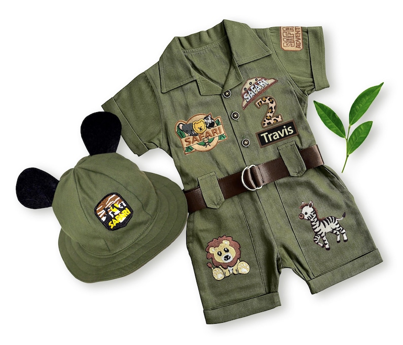 Front view of a personalized olive green safari costume for kids featuring custom "Travis" name and age "2" patches. The set includes a matching green hat with cute black ears, perfect for a Wild One birthday outfit or jungle-themed Halloween costume.