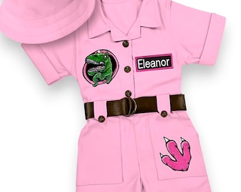 May include: Pink dinosaur costume set with a matching bucket hat. The short-sleeved jumpsuit features a brown belt, a green dinosaur patch, a pink dinosaur footprint, and the name "Eleanor".