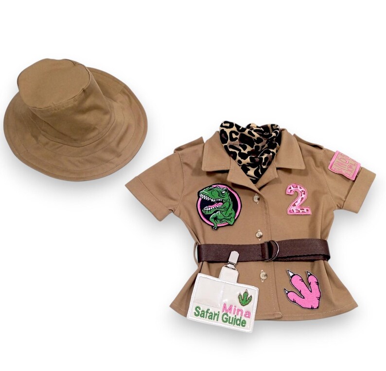 Puede incluir: Un atuendo de safari color canela con un sombrero a juego. El atuendo incluye una camisa de manga corta con parches, un cintur&oacute;n y una etiqueta con el texto "Mina Safari Guide". Se incluye una bufanda con estampado de leopardo.
