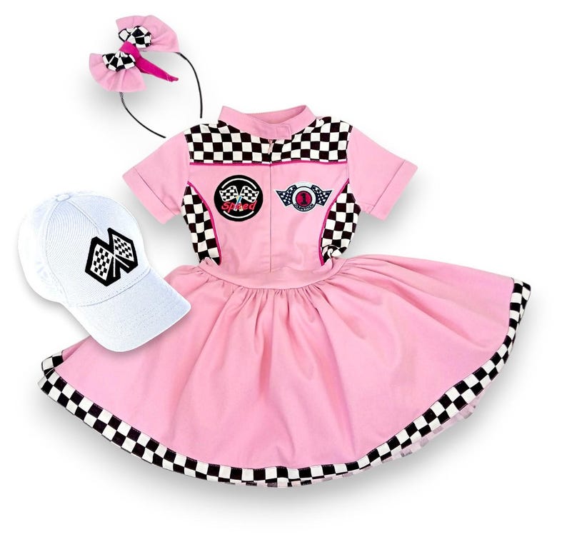 May include: A pink and white checkered racing-themed dress with a white cap and a pink headband. The dress has a black and white checkered trim and a white collar. The cap has a black and white checkered flag design. The headband has a pink bow.