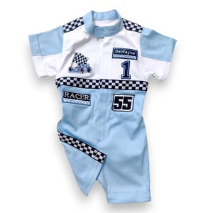May include: A light blue racing jumpsuit with black and white checkered trim. The jumpsuit has patches that say "DeWayne", "Racer", and "55". There is also a patch with a cartoon race car.